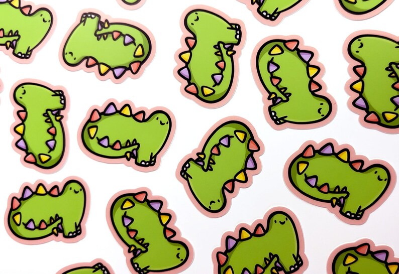 Op de afbeelding: Een set van 12 groene dinosaurus stickers met roze contouren en kleurrijke accenten. Elke dinosaurus heeft een glimlachend gezicht en een staart met een rij kleurrijke driehoeken.