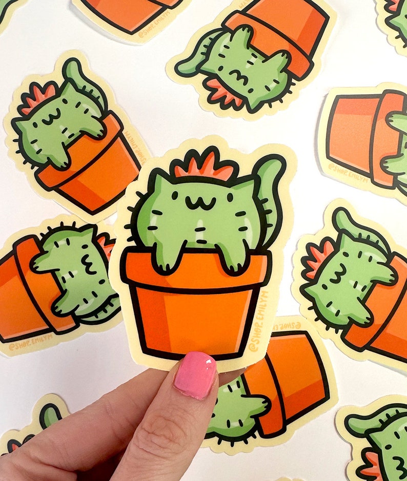May include: A set of stickers featuring a cartoon cat dressed as a cactus in a terracotta pot. The cat is green with a red crown and a white face. The stickers are on a white background and have the text "@shop.earthly" on them.
