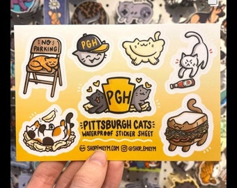 Puede incluir: Una hoja de pegatinas con lindos gatos de dibujos animados con diseños de Pittsburgh. La hoja incluye un gato con un sombrero "PGH", un gato durmiendo en una señal de "No estacionar", un gato comiendo un pierogi, un gato con un sándwich y un gato con una botella de ketchup. El texto "Pittsburgh Cats Waterproof Sticker Sheet" está impreso en la hoja.