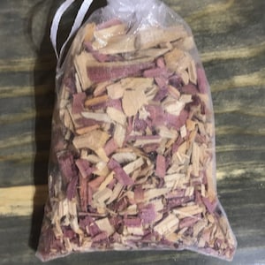 May include: A small, sheer mesh bag filled with wood chips. The chips are a mix of light tan and reddish-purple, creating a natural, earthy appearance. The bag is tied at the top with a white drawstring.
