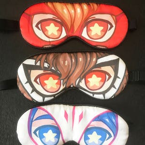 May include: Three sleep masks with different character designs. Each mask has a pair of large eyes with a yellow star in the center. The top mask is red with a brown haired character. The middle mask is brown with a brown haired character. The bottom mask is white with a blue haired character.
