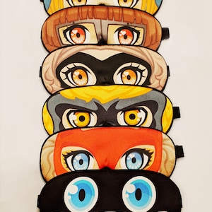May include: Six colorful sleep masks with different cartoon characters. Each mask features large eyes and a unique design.