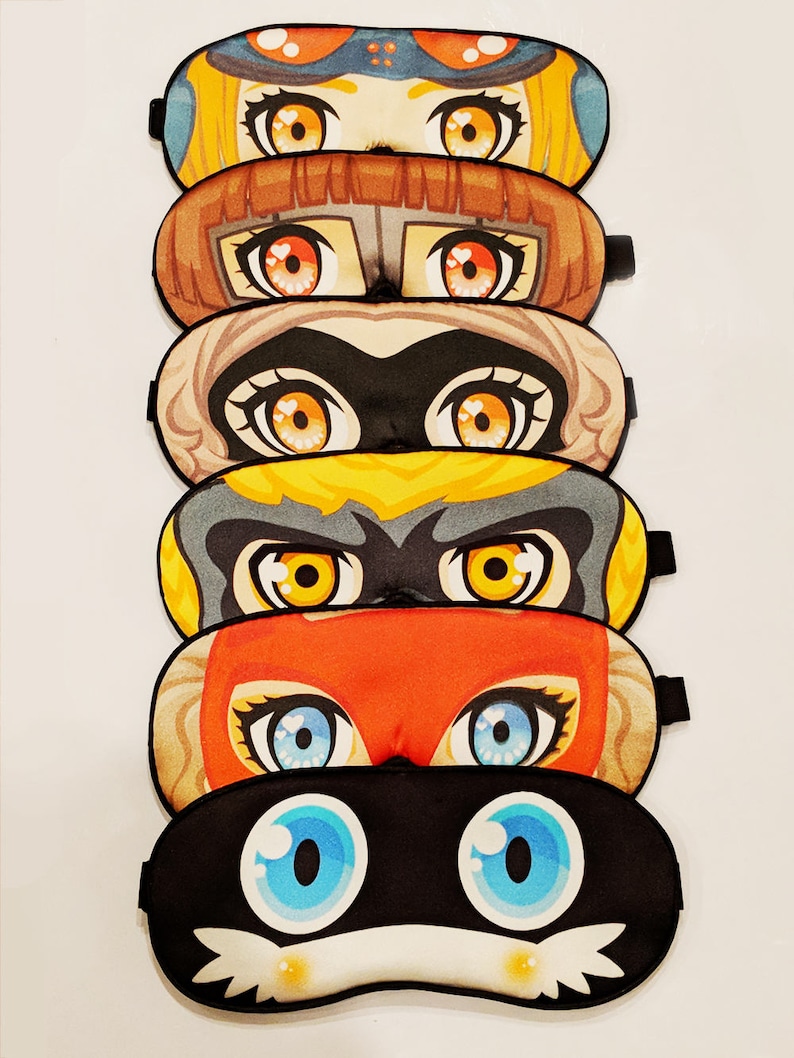 May include: Six colorful sleep masks with different cartoon characters. Each mask features large eyes and a unique design.
