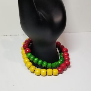 May include: A set of three wooden bracelets with red, green, and yellow beads. The bracelets are stacked on top of each other.