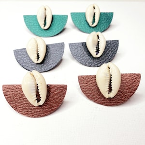 May include: Six pairs of earrings featuring cowrie shells on leather half-circle shapes. The earrings are in three colors: green, black, and brown.