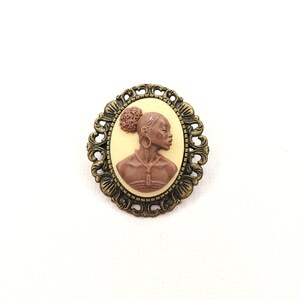 May include: A brown cameo brooch with a detailed profile of a woman with a bun in her hair. The cameo is set in a brass-toned ornate metal frame.