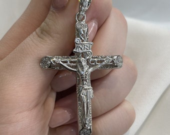 May include: A silver cross pendant with a detailed design and small clear stones. The cross features a figure of Jesus Christ.