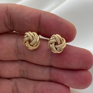 Puede incluir: Un par de pendientes de oro en forma de nudo. Los pendientes son peque&ntilde;os y delicados, y tienen una superficie texturizada.