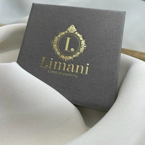 Puede incluir: Una caja gris con un logotipo dorado que dice "L. Limani Joyer&iacute;a Cl&aacute;sica".