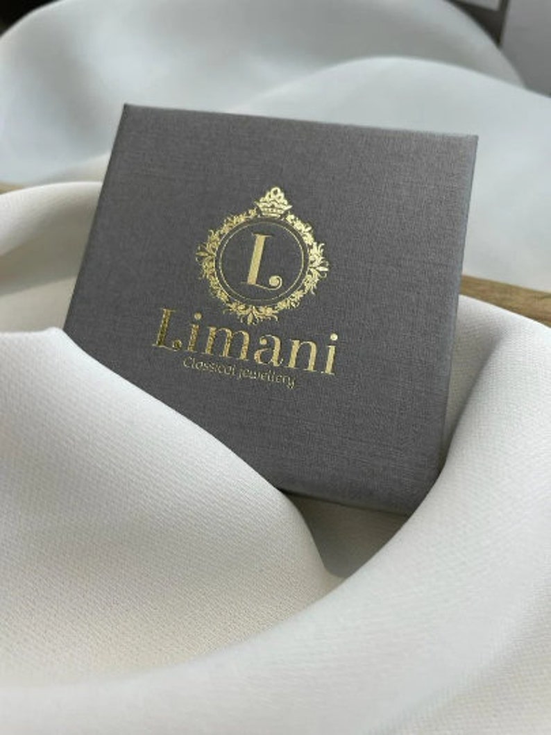 Puede incluir: Una caja gris con un logotipo dorado que dice "L. Limani Joyer&iacute;a Cl&aacute;sica".