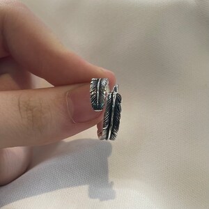 May include: A silver ring with a feather design. The ring is open and adjustable.