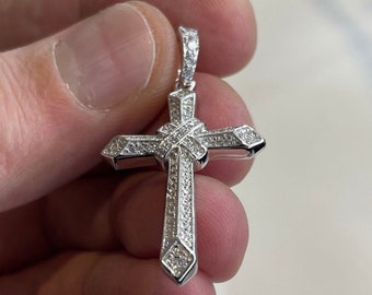 May include: A silver cross pendant with a detailed design and small clear stones set into the metal.