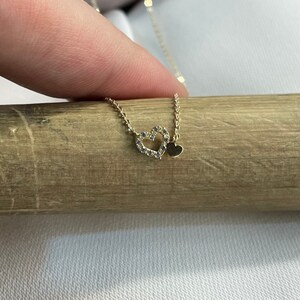 May include: A gold necklace with two heart pendants. The larger heart is open and has small clear stones around the edge. The smaller heart is solid and sits inside the larger heart.