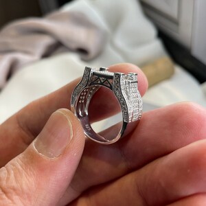 May include: A silver ring with a square-shaped setting and a band encrusted with small, clear stones. The ring is marked "925" on the inside.