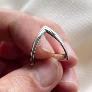 Puede incluir: Un anillo de plata con forma de V, con un acabado liso y pulido.