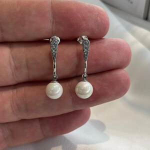 May include: A pair of silver dangle earrings with a pearl drop and clear cubic zirconia accents.