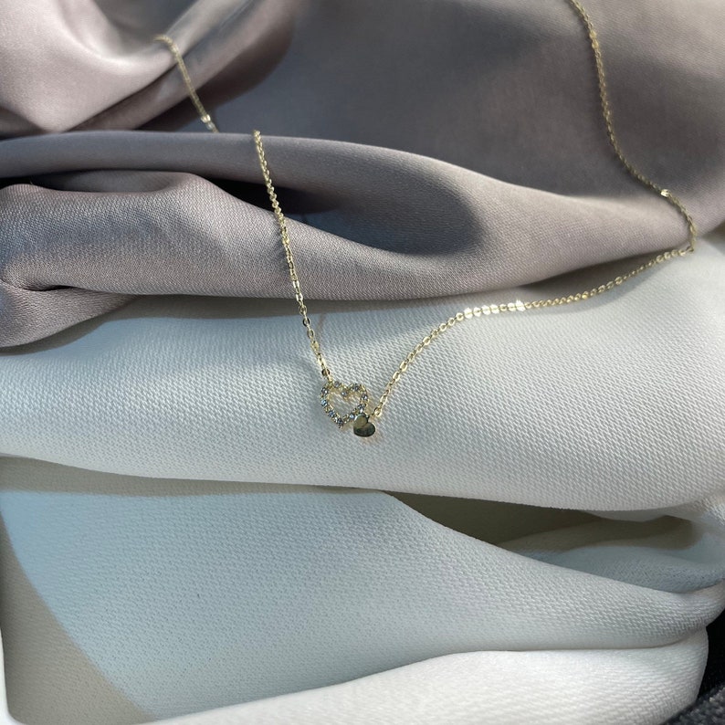 May include: A delicate gold necklace featuring a double heart pendant. The heart is embellished with small sparkling stones.