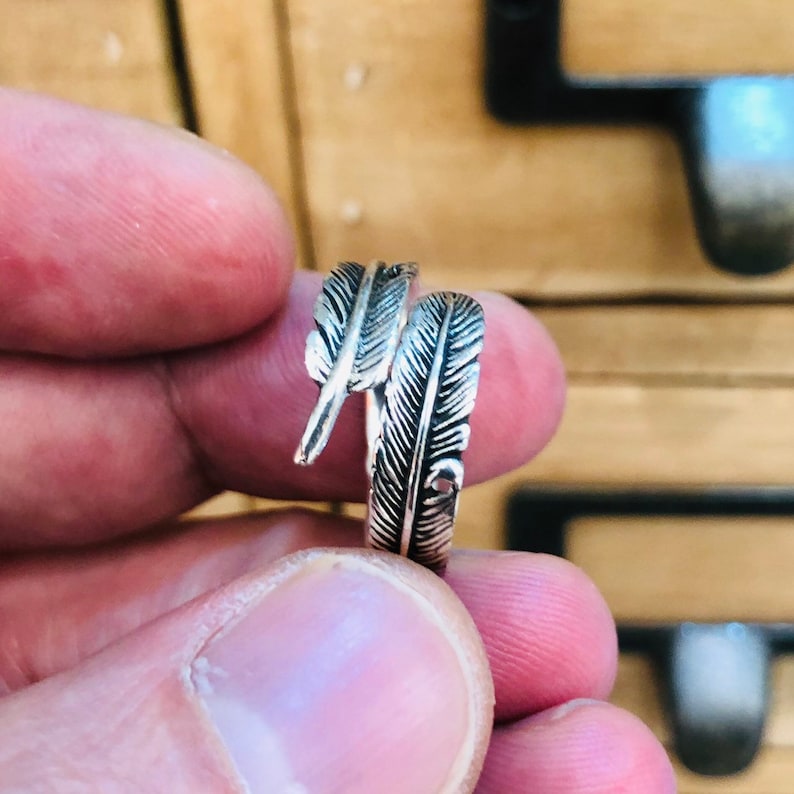 Puede incluir: Un anillo de plata con un dise&ntilde;o de dos plumas entrelazadas.