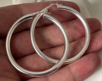 May include: A pair of silver hoop earrings. The hoops are thick and round, and they are made of a smooth metal.
