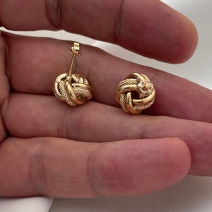 Puede incluir: Un par de pendientes de oro en forma de nudo. Los pendientes son peque&ntilde;os y delicados, y tienen un dise&ntilde;o simple y elegante.