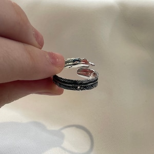 May include: Silver ring with a feather design. The ring is open and has a textured finish.