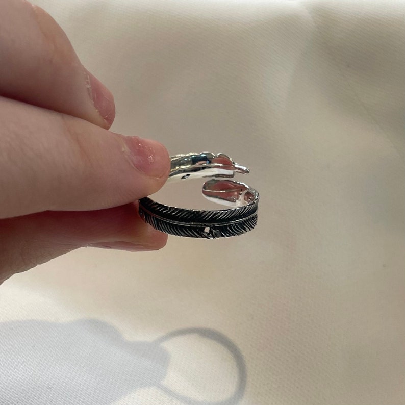 May include: Silver ring with a feather design. The ring is open and has a textured finish.