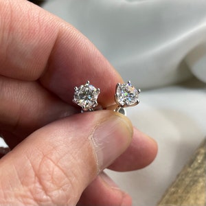 Op de afbeelding: Een paar zilveren oorbel studs met ronde, heldere, glinsterende stenen gezet in een zes-klauw setting.