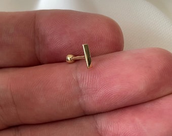 May include: Gold bar stud earring with a small ball at the end. The bar is about 6 mm long.