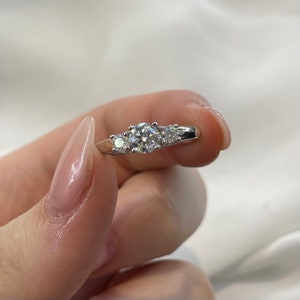 Puede incluir: Un anillo de plata con tres diamantes redondos. El diamante central es m&aacute;s grande que los dos diamantes a cada lado.