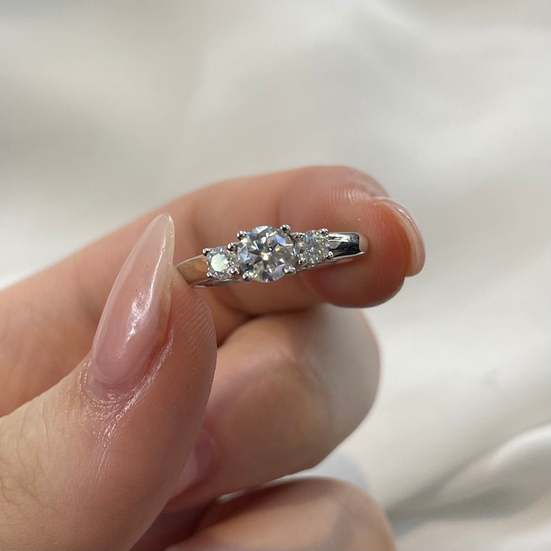 Puede incluir: Un anillo de plata con tres diamantes redondos. El diamante central es m&aacute;s grande que los dos diamantes a cada lado.