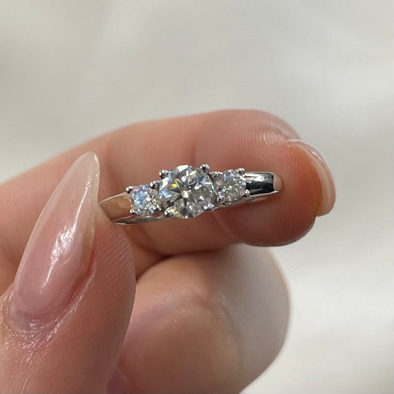 Puede incluir: Un anillo de plata con un gran diamante redondo en el centro y dos diamantes m&aacute;s peque&ntilde;os a cada lado.