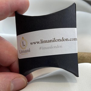 Pu&ograve; includere: Una scatola a cuscino nera con un'etichetta bianca che dice "www.limanilondon.com" e "#limanilondon". L'etichetta presenta anche un logo dorato con la lettera "L" e la parola "Limani".