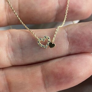 May include: A gold chain necklace with a delicate heart pendant. The heart is outlined with small sparkling stones and has a smaller solid heart charm hanging from it.