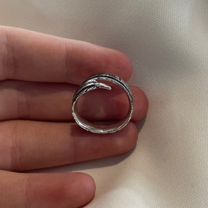 May include: A silver ring with a feather design. The feather is wrapped around the band of the ring.