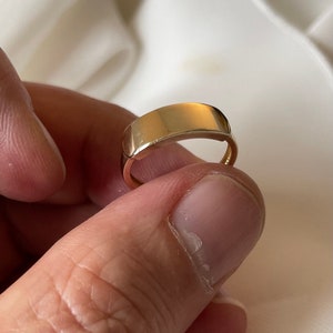 May include: A simple gold band ring with a flat, smooth top.