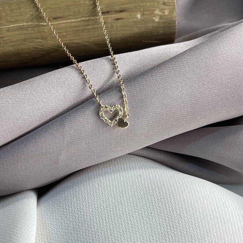 May include: A gold necklace with a delicate heart pendant. The heart is made of small, sparkling stones.