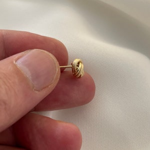 May include: A gold knot-shaped earring with a textured surface.