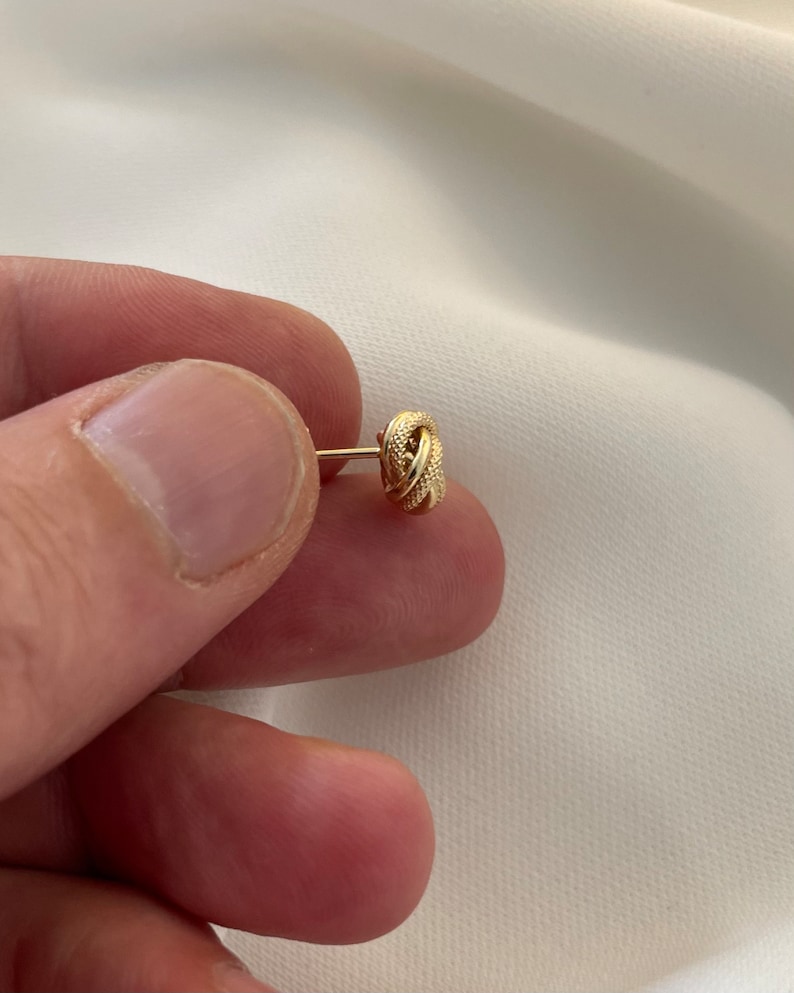 May include: A gold knot-shaped earring with a textured surface.