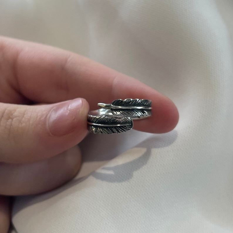May include: A silver ring with a feather design. The ring is adjustable and can be worn on any finger.