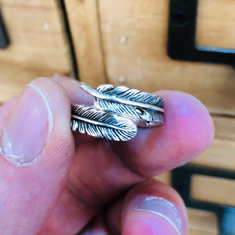 Puede incluir: Un anillo de plata con un dise&ntilde;o de dos plumas superpuestas.