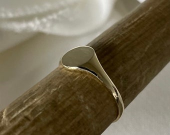 May include: A gold signet ring with a smooth, oval-shaped top.