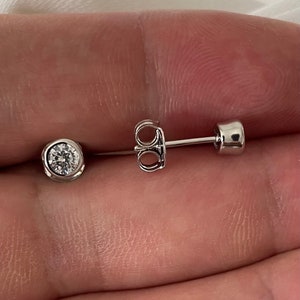 Op de afbeelding: Een paar zilveren oorbelletjes met elk een enkele ronde, heldere edelsteen.