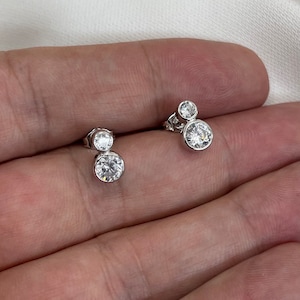 May include: A pair of silver earrings with two clear round cubic zirconia stones on each earring.