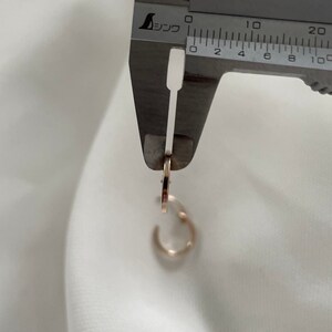 May include: A close-up of a gold hoop earring being measured with a silver caliper. The caliper reads 10 mm.