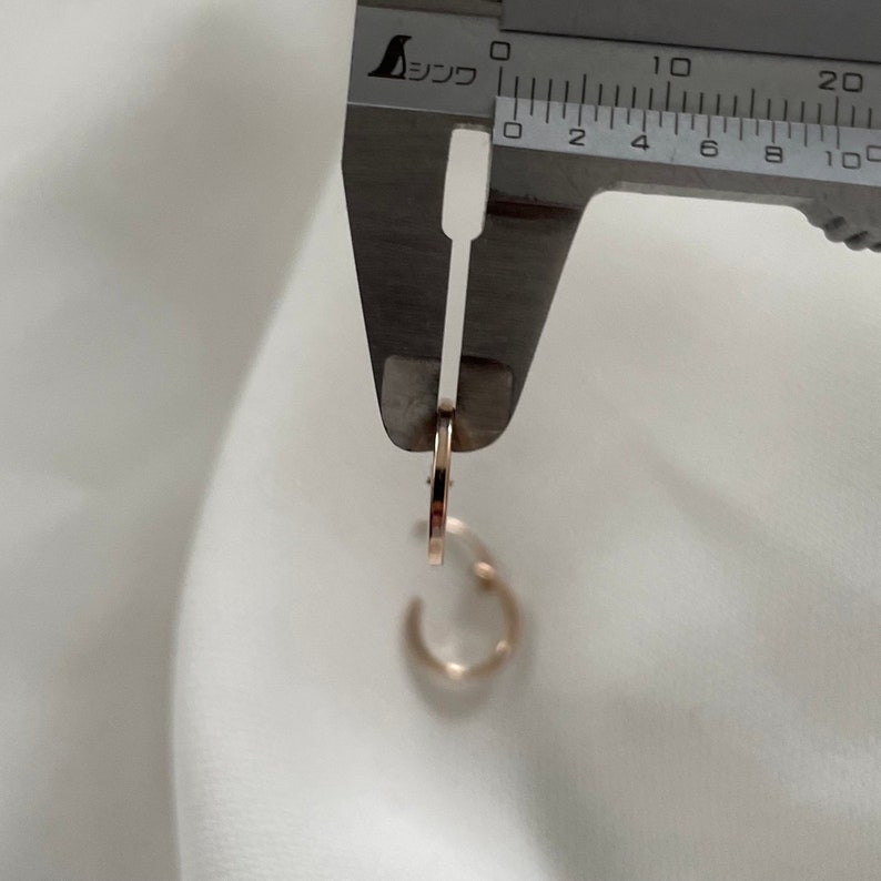 May include: A close-up of a gold hoop earring being measured with a silver caliper. The caliper reads 10 mm.