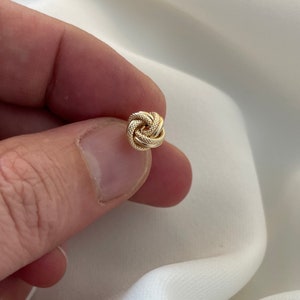 May include: A gold knot earring with a textured surface.