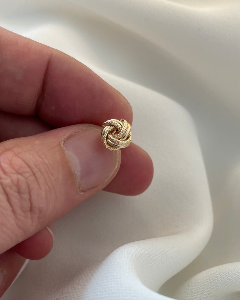 May include: A gold knot earring with a textured surface.