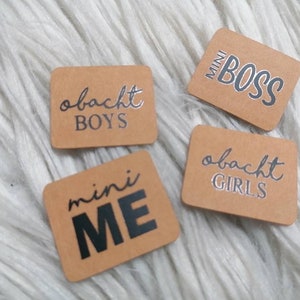 Könnte beinhalten: Vier braune rechteckige Etiketten mit weißem Text. Die Etiketten lauten "mini boss", "mini ich", "obacht boys" und "obacht girls".
