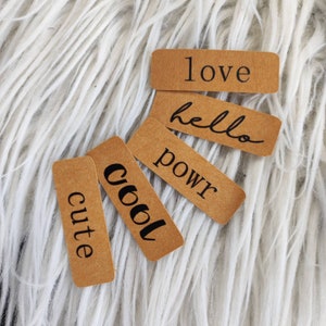 Könnte beinhalten: Fünf braune Papieretiketten mit schwarzem Text. Die Etiketten sagen "love", "hello", "power", "cool" und "cute".