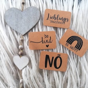 Puede incluir: Cinco tarjetas de papel marrón con texto y gráficos negros. Las tarjetas dicen "Lieblingsmensch", "be kind", "BE HAPPY" con un gráfico de arcoíris, "NÖ" y un pequeño corazón.